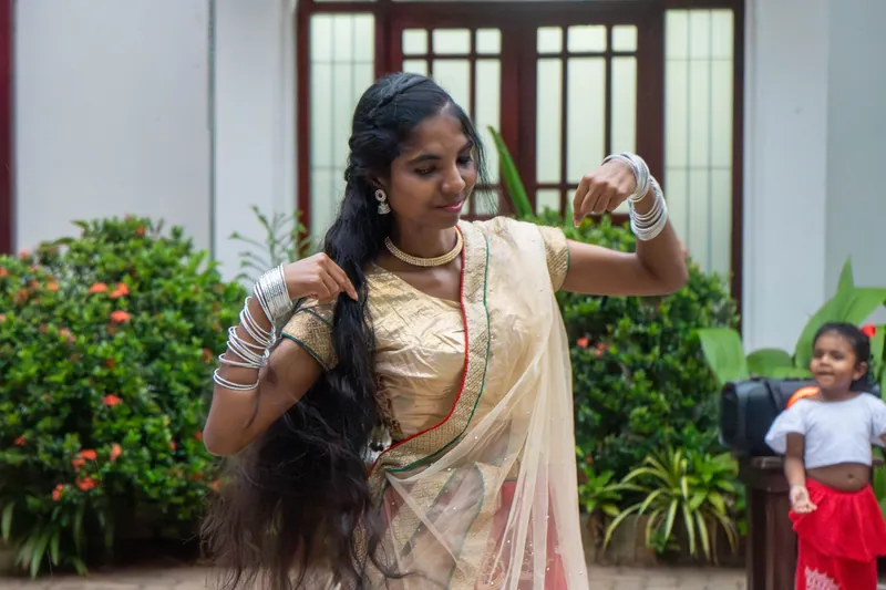 A young dancer in traditional dress performs in the garden while a small child watches