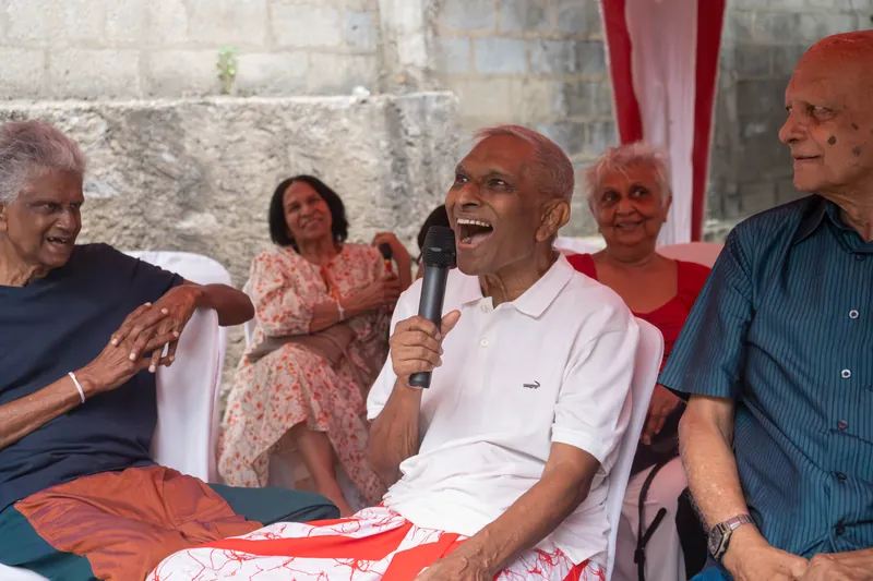 A resident laughing into a microphone during the biggest-laugh competition, friends gathered around him