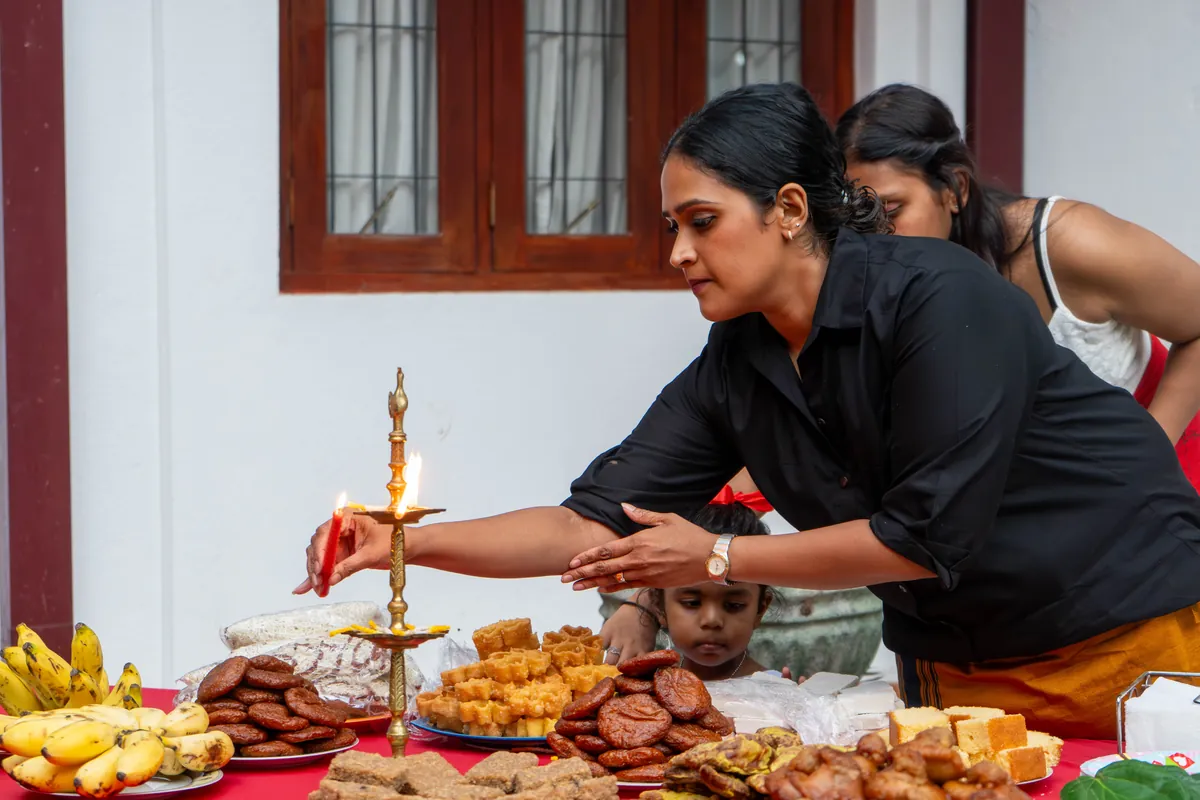 A woman lights the traditional brass oil lamp over a table of New Year sweets