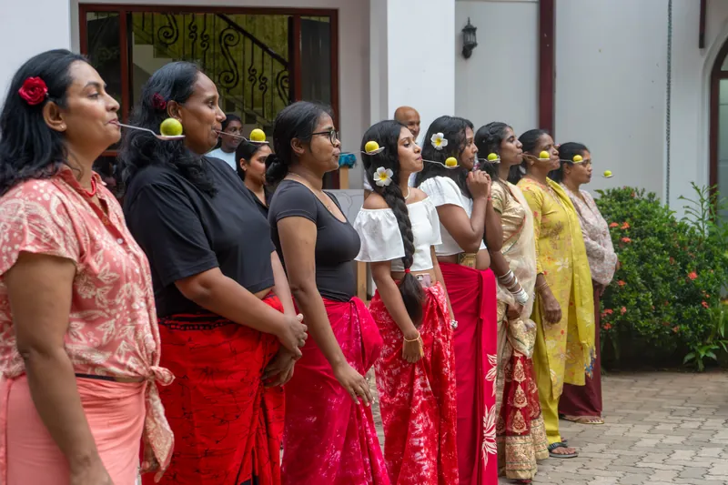 A line of women in festive dress waiting to start with limes balanced on spoons in their mouths