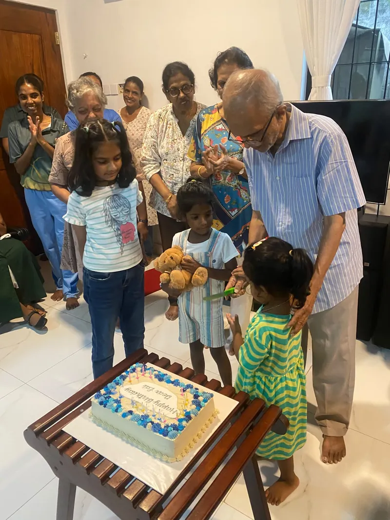 Children watch closely as an elderly resident cuts his birthday cake
