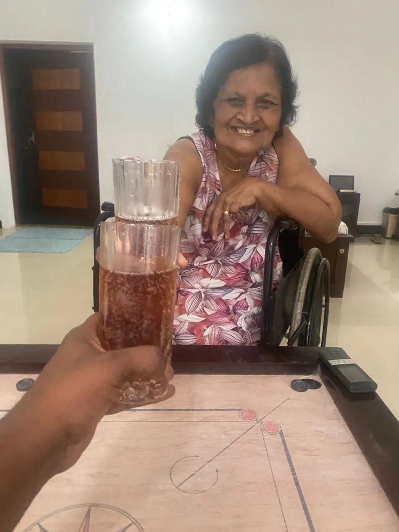 A smiling resident in a wheelchair raising a glass over a carrom board
