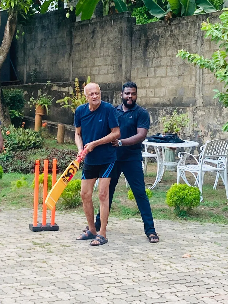 Dr. Vasika helps a resident hold a cricket bat at the wicket in the garden