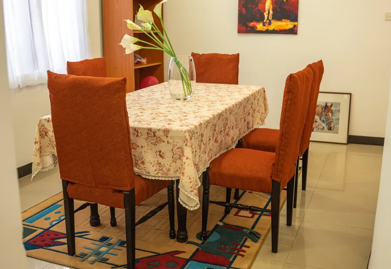 The dining room with orange upholstered chairs, a floral tablecloth and fresh flowers on the table