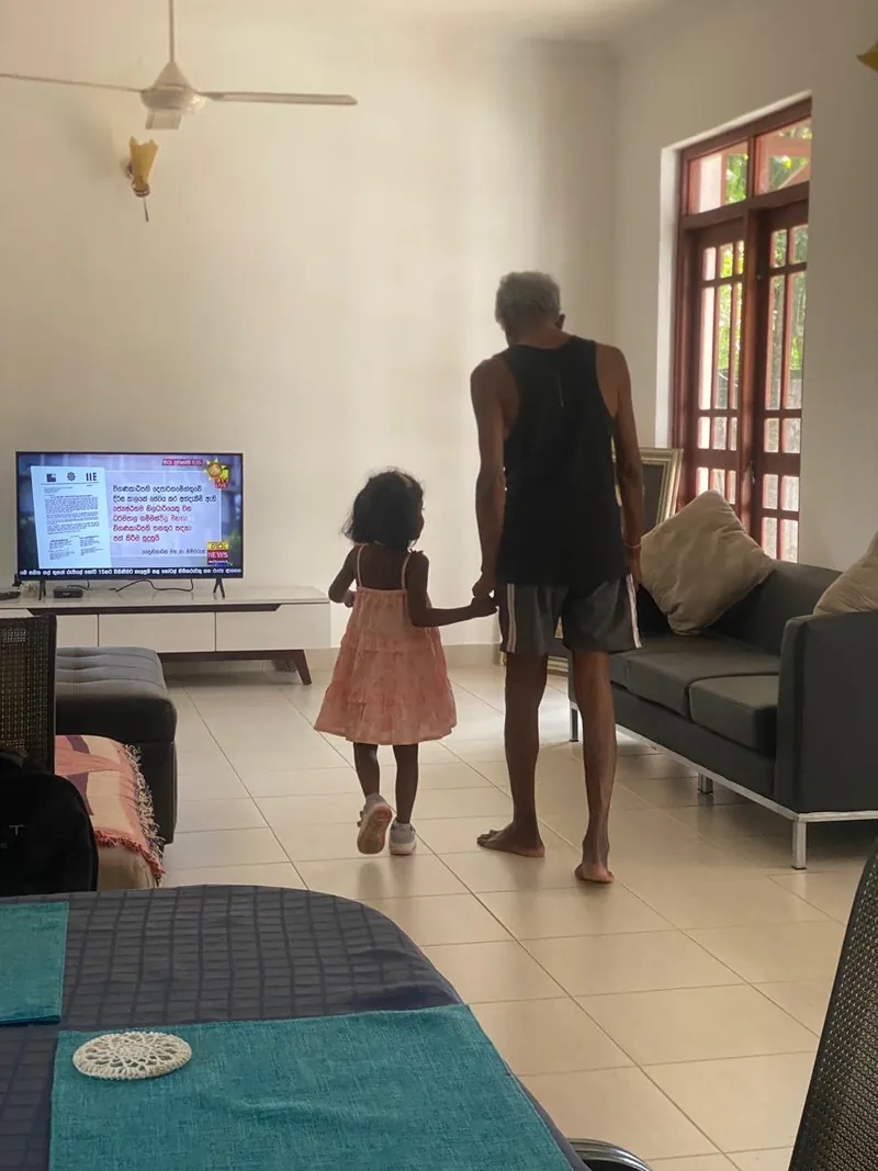 An elderly resident walks hand in hand with a small child in the living room