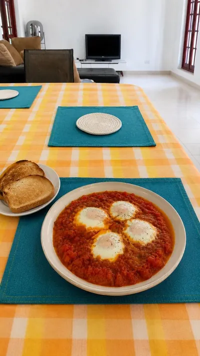 A dish of shakshuka — eggs poached in spiced tomato sauce — with toast on a set table