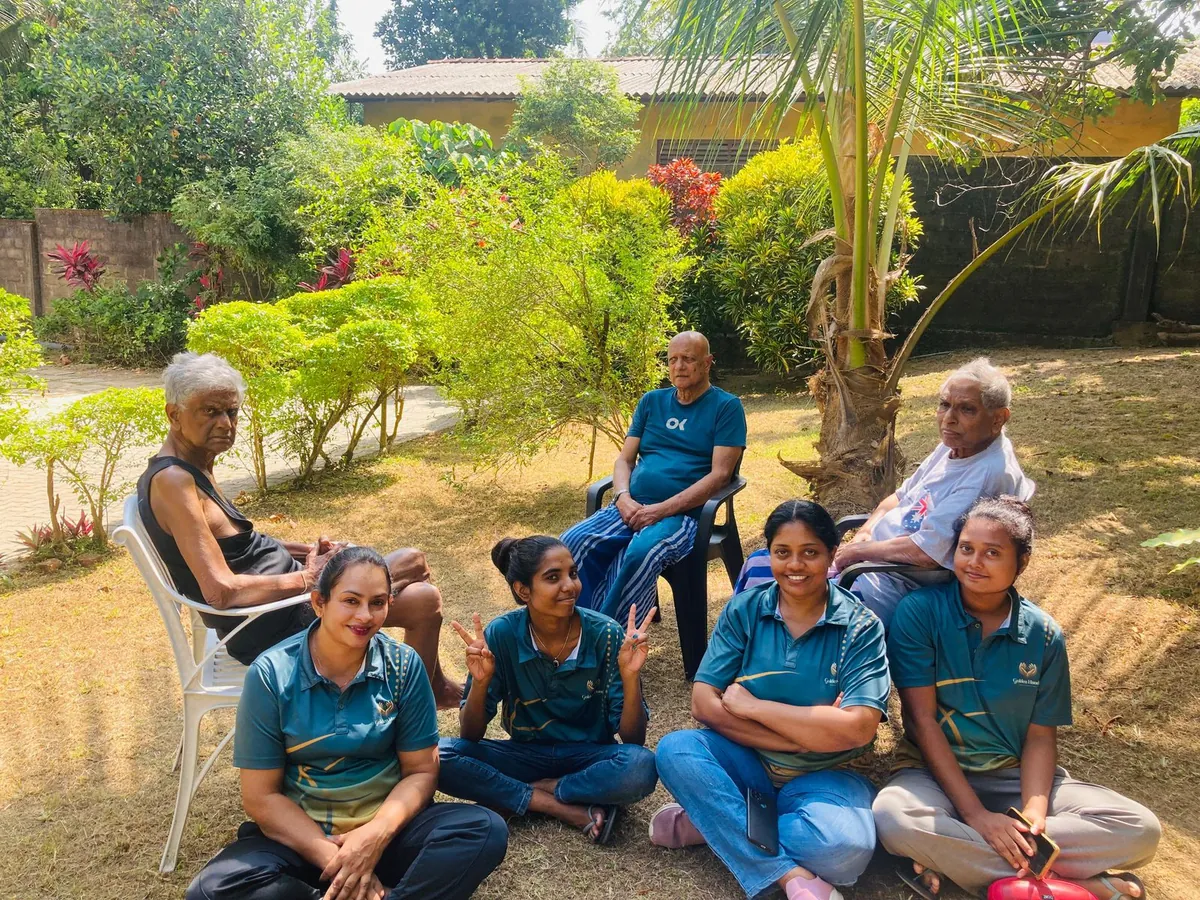 Four caregivers sitting on the grass with three residents behind them in the garden