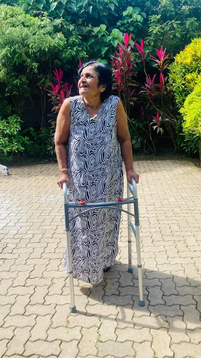 A resident with a walking frame smiling among bright garden flowers