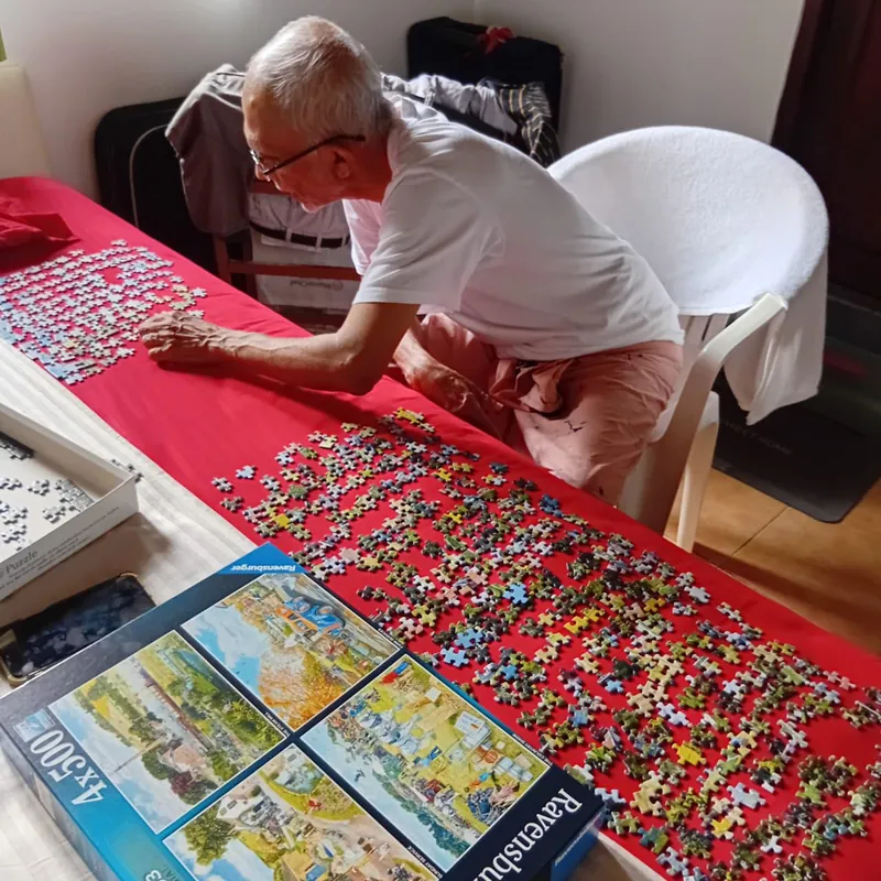 An elderly resident working on a large jigsaw puzzle at a long table