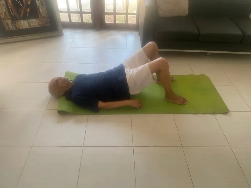 A resident doing a gentle bridge exercise on a green mat in the living room