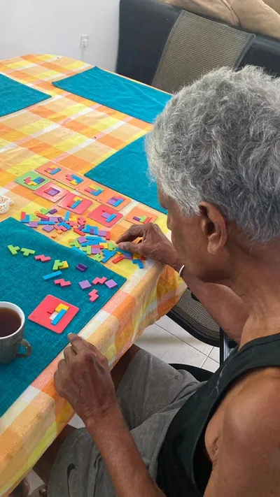 Seen from behind, a resident arranges puzzle pieces beside a cup of tea