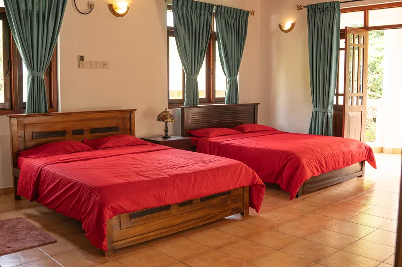 A bright twin bedroom with wooden beds, red bedspreads and garden windows