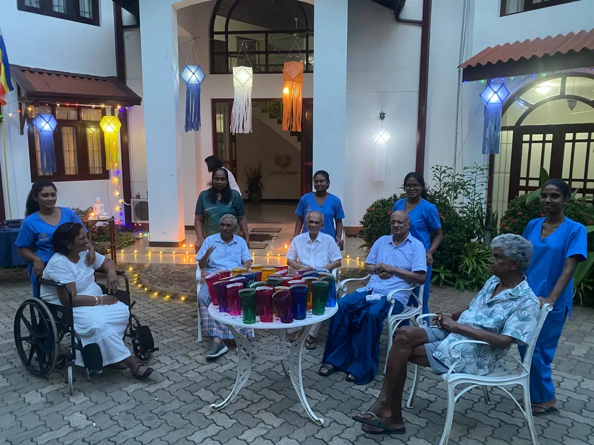 Residents and caregivers gathered around a table of lanterns in the lamplit courtyard at dusk