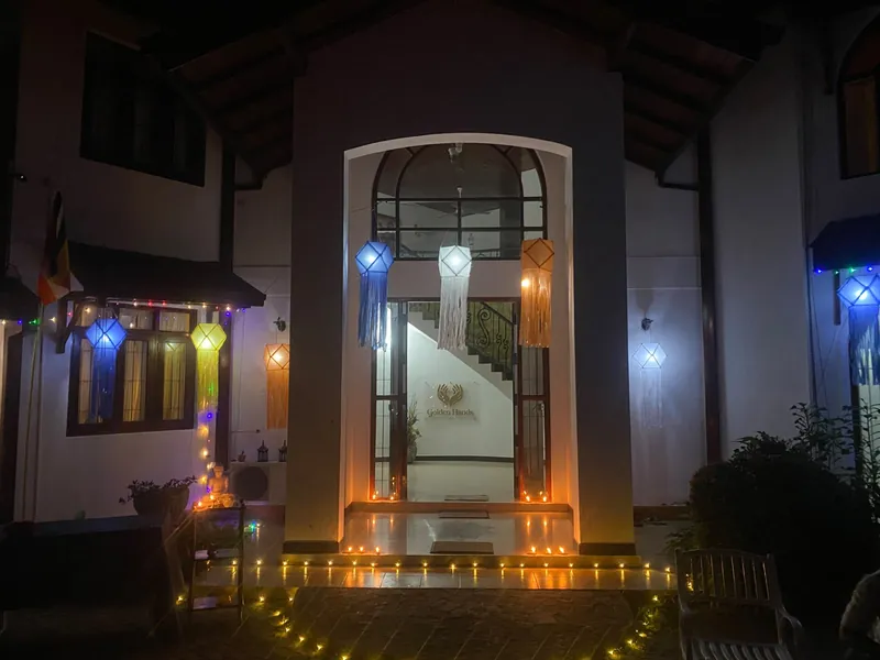 The home's entrance at night decorated with Vesak lanterns and rows of oil lamps