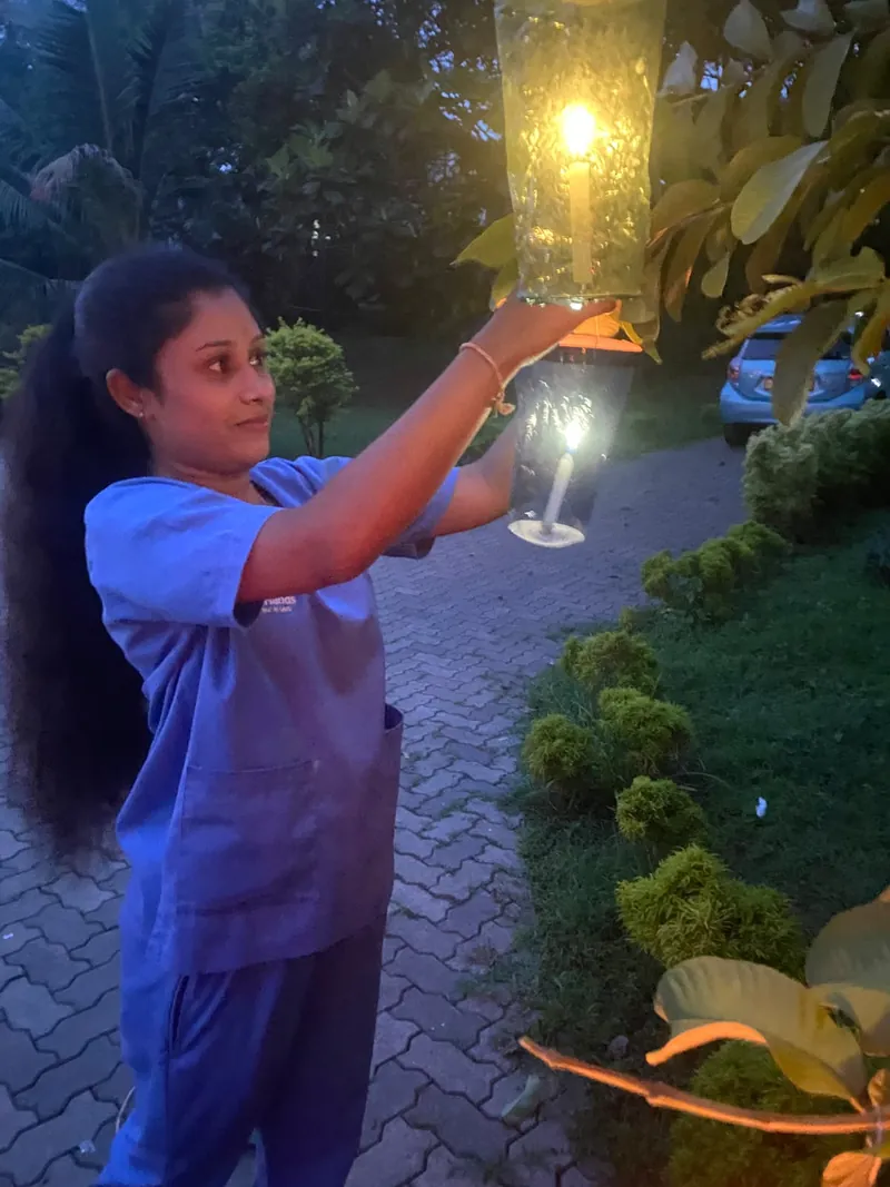 A resident in a wheelchair beneath a tree strung with glowing paper lanterns at night