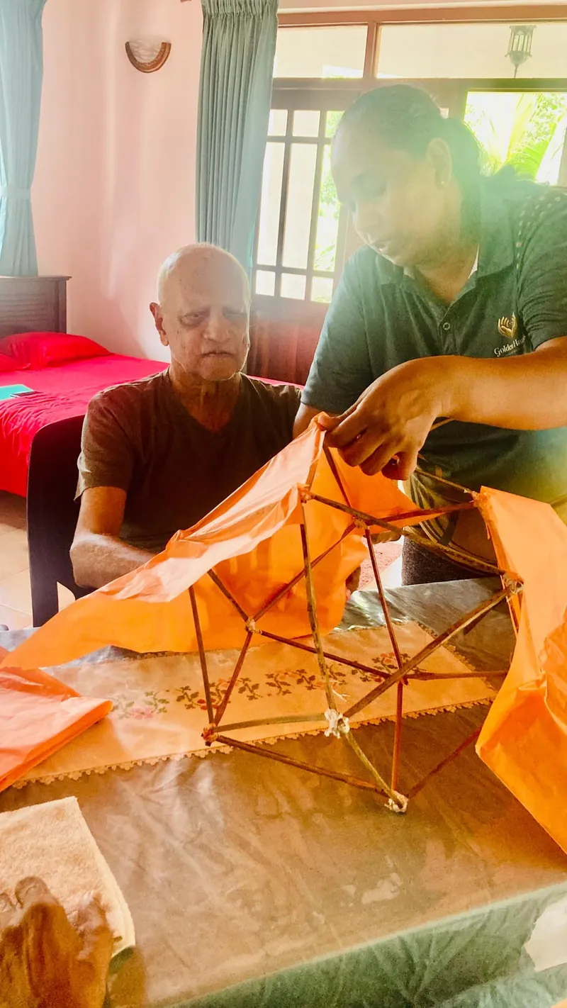 A caregiver and resident stretch orange tissue over a lantern frame