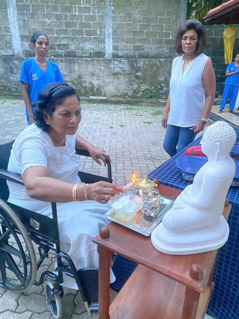 A resident in white lights an oil lamp at a small Buddha shrine