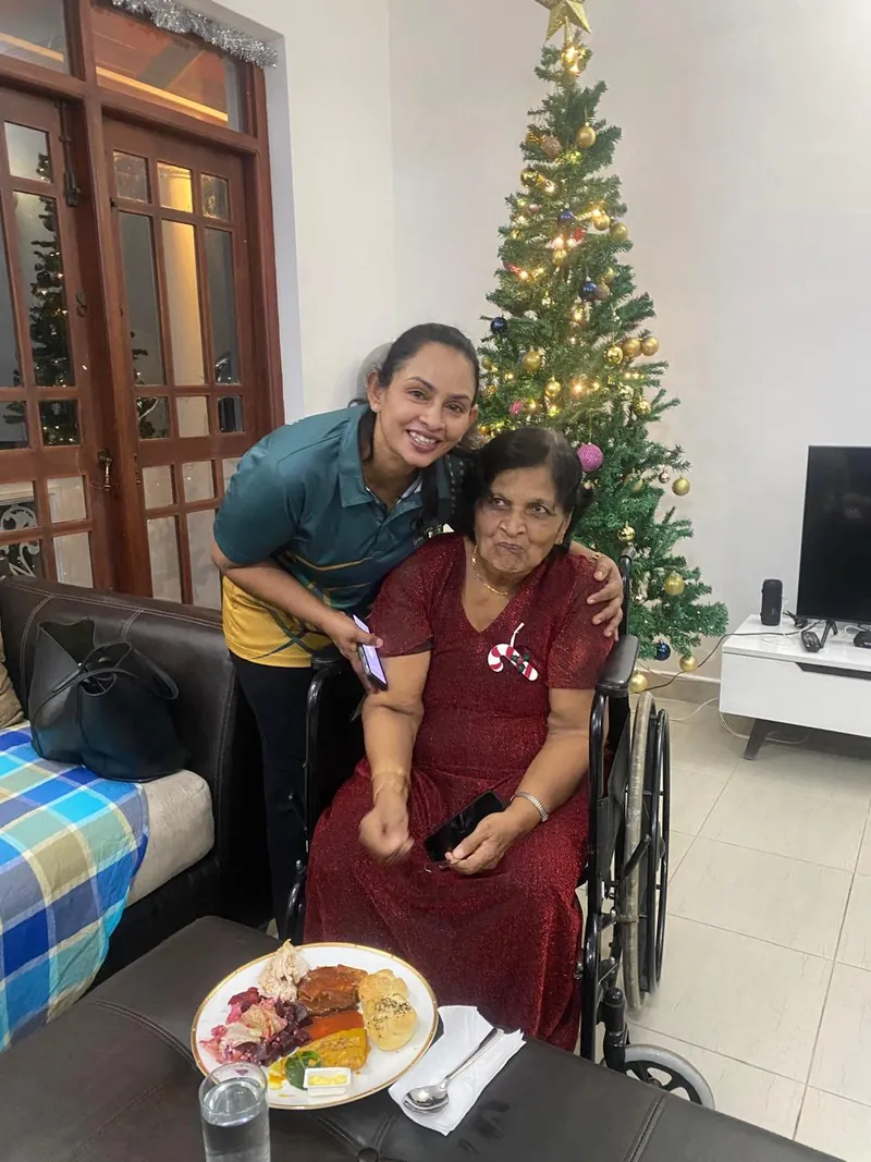 A caregiver embraces a resident in a red dress beside the Christmas tree